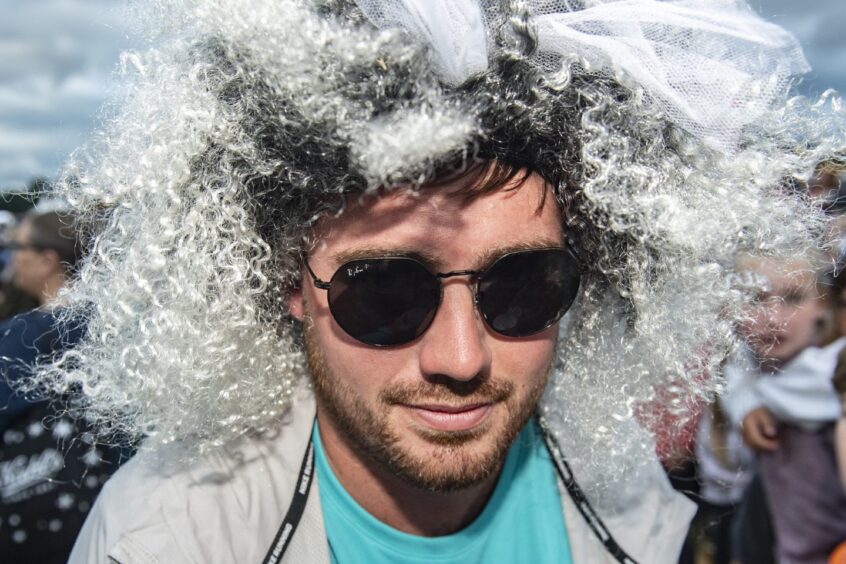 A frizzy black and white wig surrounds the face and sunglasses of this festivalgoer in the crowd.