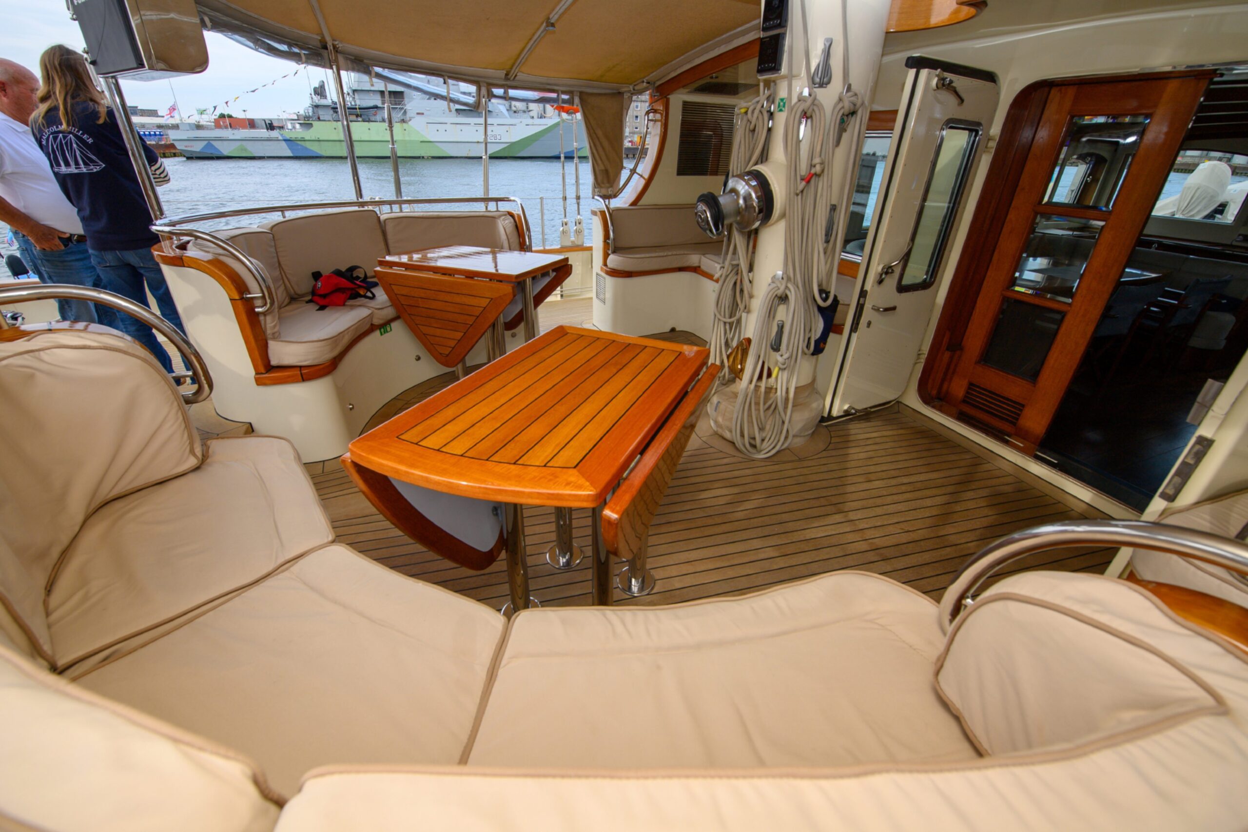 The seating area of the Malcolm Miller, with two arched sofas with cream cushions, two wooden tables and wooden doors leading to the interior of the vessel.