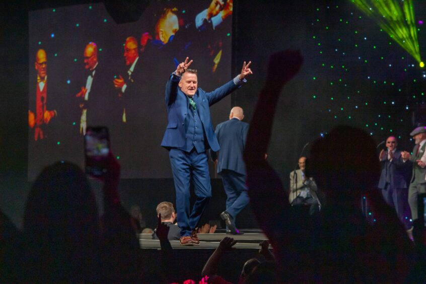 A male model from the Brave event salutes the crowd from the stage.
