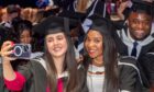 A student takes a selfie with her fellow graduate in the crowd.