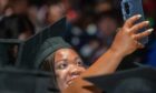 Graduate in mortarboard smiling and holding up a phone for a selfie.