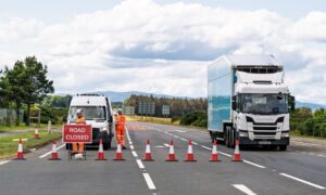 Red road closed sign with cones and a HGV and van sitting behind the cones.