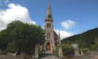 A picture of Ballater Old Kirk, with a church spire and trees in the foreground.