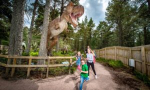 Family running along forest path, below a dinosaur statue with its mouth gaping open