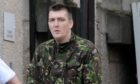 A man in a camouflage jacket looks at the camera.