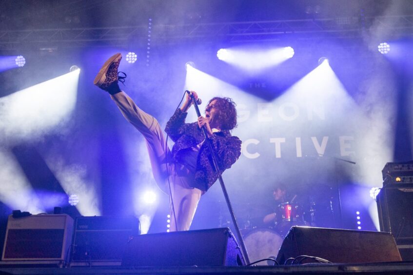 A singer at the microphone kicks his leg high in the air on stage with The Pigeon Detectives.