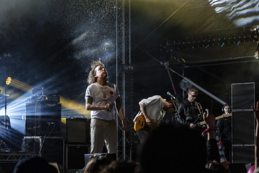 Singer of The Pigeon Detectives stands in a spotlight as droplets of water fall on him from above.