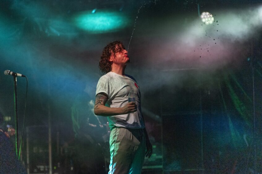 Lead singer of The Pigeon Detectives blows water into the air which he's taken from a plastic bottle in his hand..