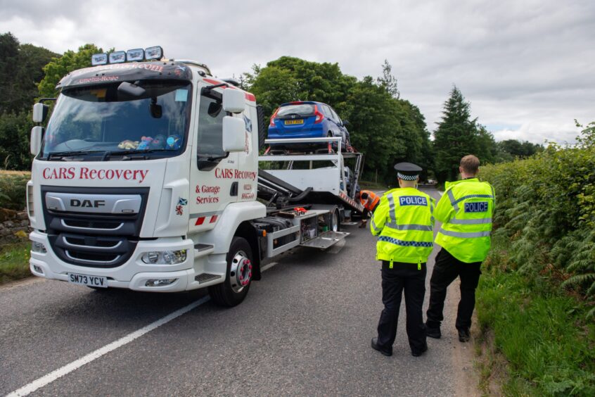 Cars on the back of a car recovery lorry, while two police in high-viz jackets look on.