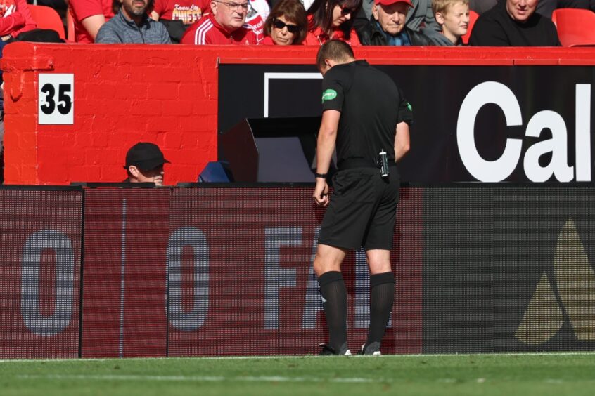 Referee Ross Hardie consults VAR before upgrading Aberdeen's Nicky Devlin's yellow card to a red. Image: SNS.