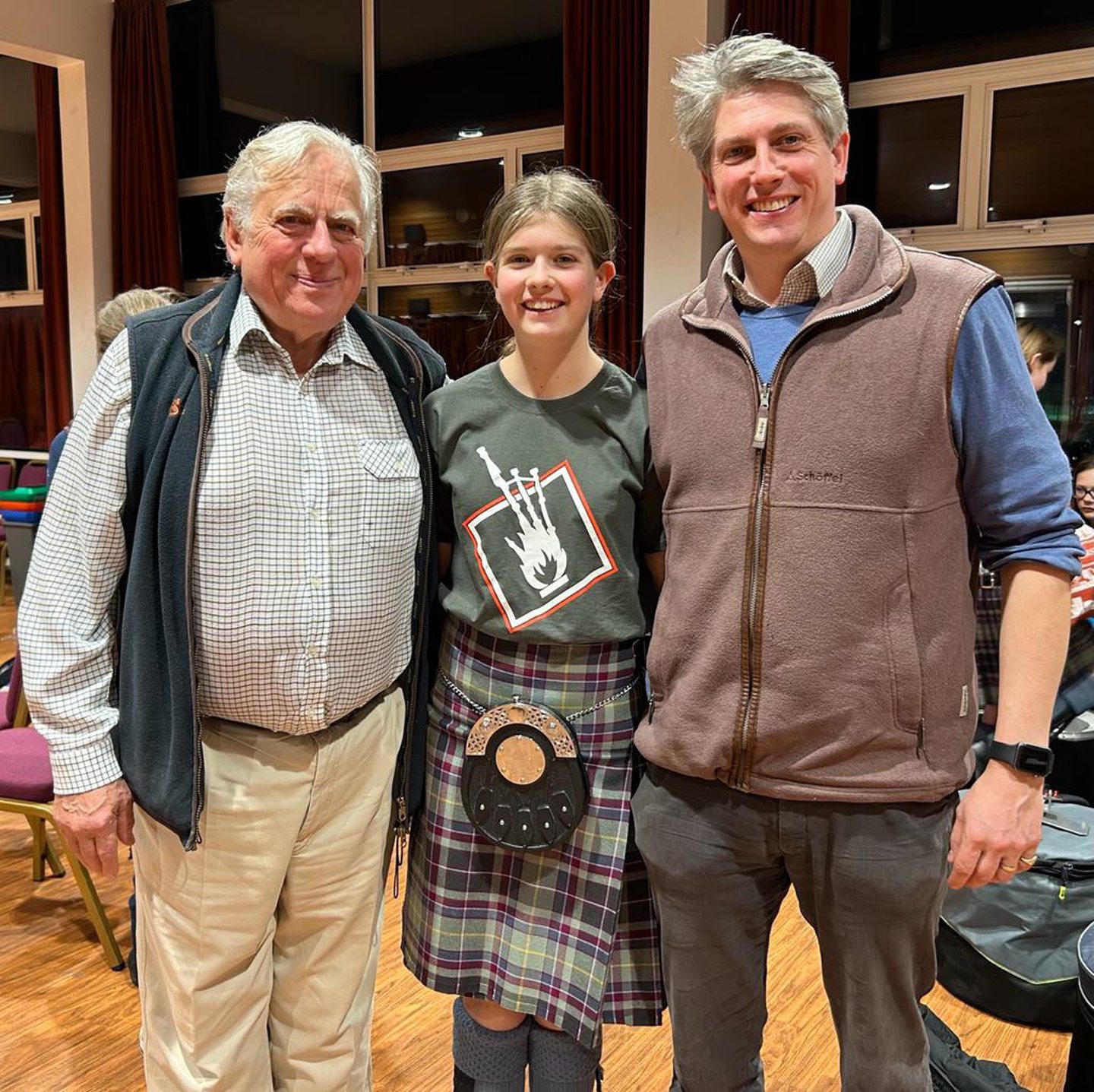 A young girl in the kilt flanked by her dad and grandfather