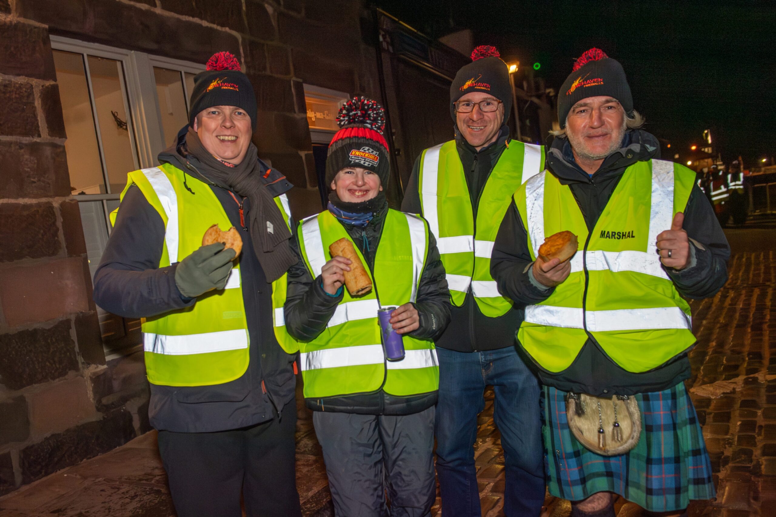 Volunteers wearing high-visibility vests eat pies during the Stonehaven Fireballs Hogmanay celebrations on Stonehaven High Street, January 1 2026.