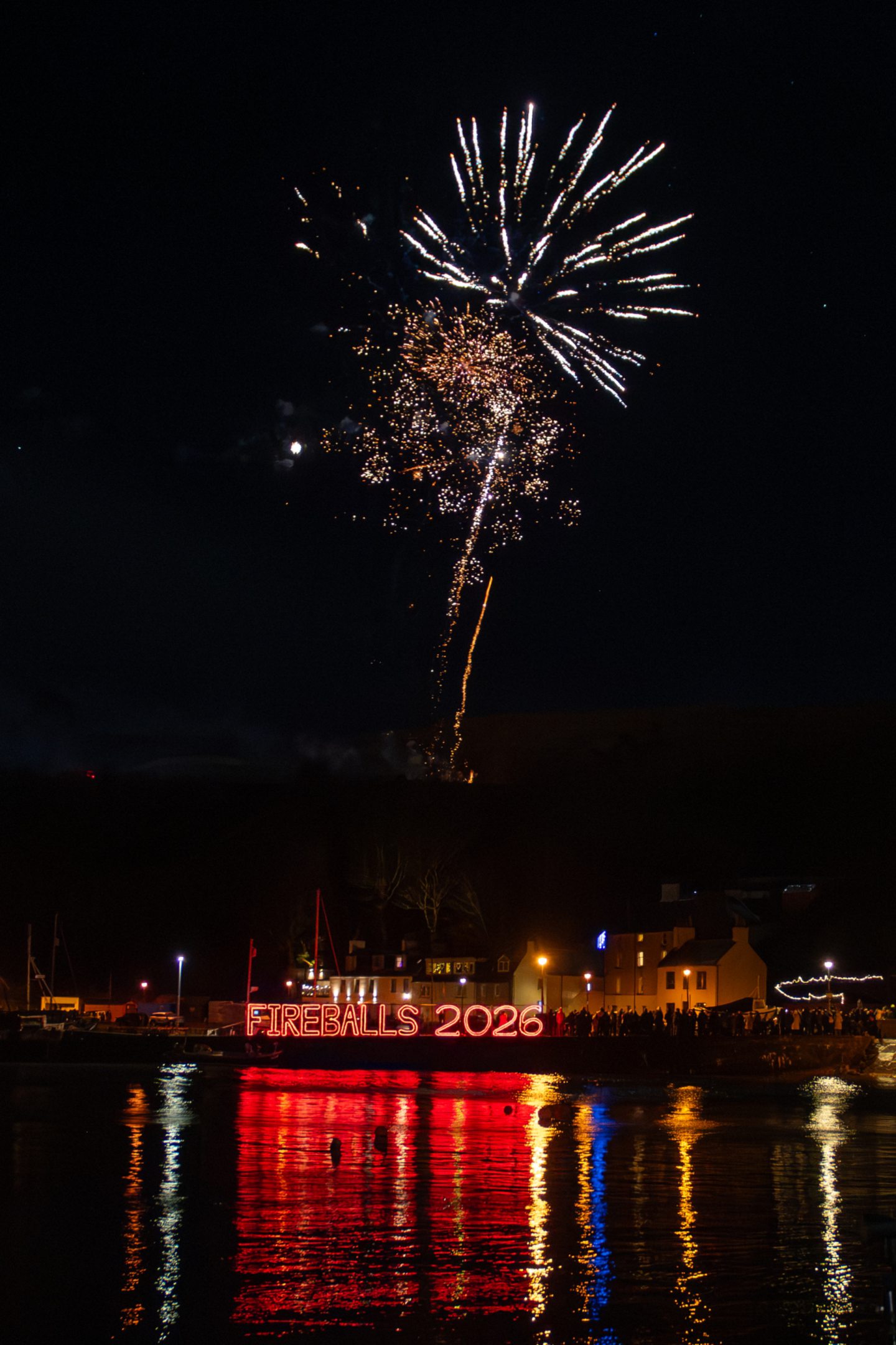 Fireworks light up the night sky above Stonehaven Harbour with the Fireballs 2026 sign reflected on the water during New Year celebrations.