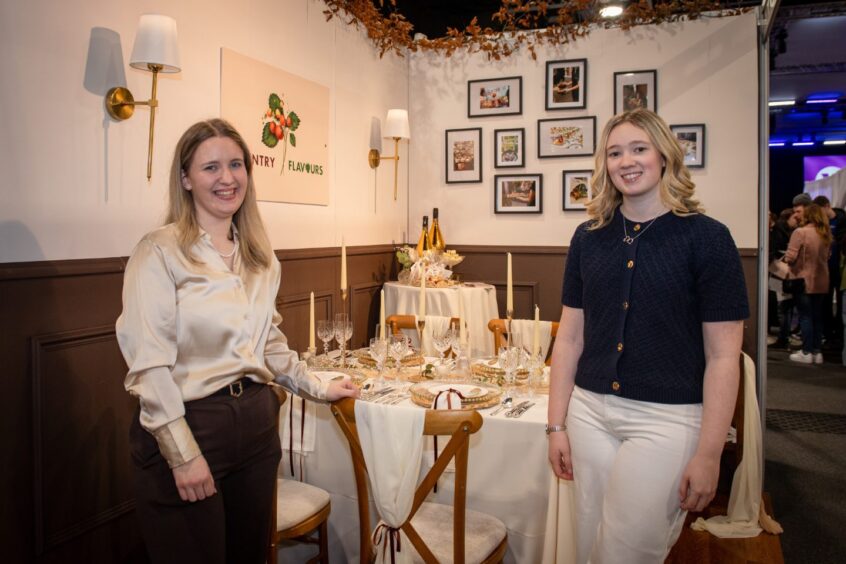 Megan Cumming and Alexandra Greig standing beside a beautifully set wedding dining display at the Country Flavours stall during the 2026 Your Wedding Exhibition in P&J Live, Aberdeen.