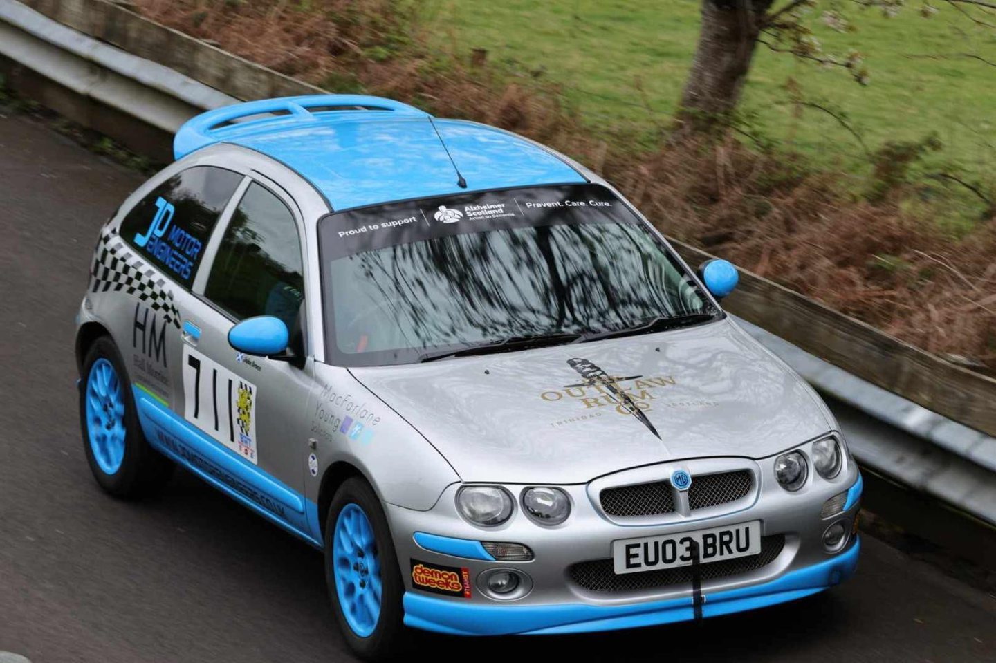 A silver MG car with light blue detail on a country road