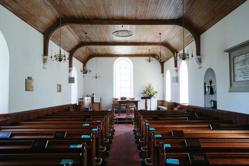 Interior of the Insh Kirk with rows of benches and a large window at the altar