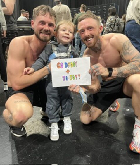 Ewan and Joel smiling with a small child at the Ironman event.