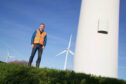 Man in orange vest stands next to wind turbine