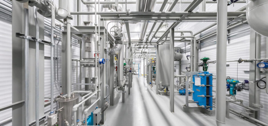 Industrial pipes in white room, with blue equipment on the right hand side