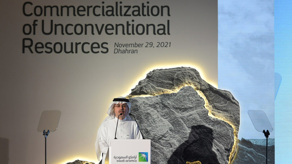 Man speaks into microphone in front of white background with "commercialization of unconventional resources" written on it