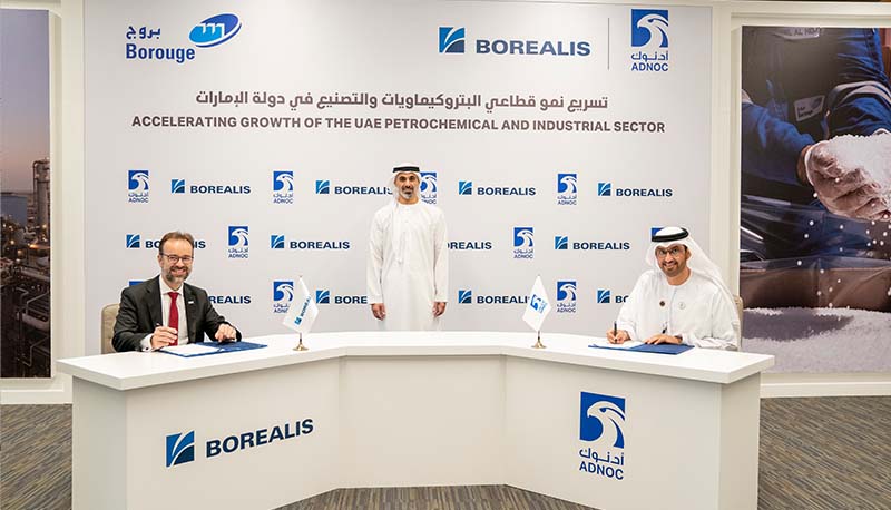 Three men behind a logoed dais smile at camera