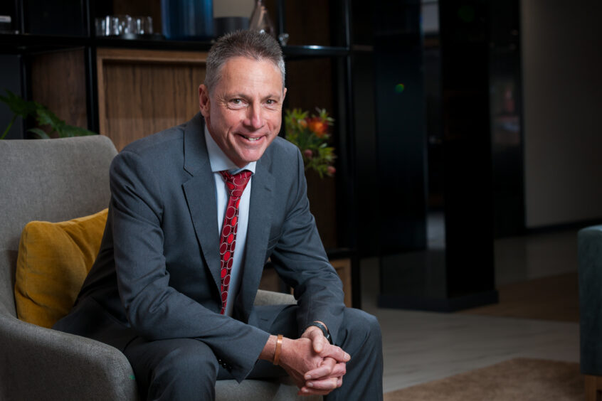 Man in suit sits on armchair looking at camera