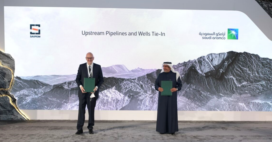 Two men stand on a stage holding green folders