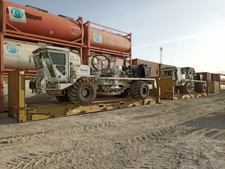 A big truck on a loader in front of some tanks