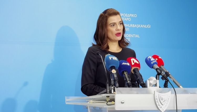 Woman talks in microphones in front of blue wall 