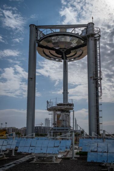 Solar tower with mirrors around bottom with sun and blue skies