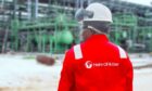 Man in red overall stands outside industrial facility