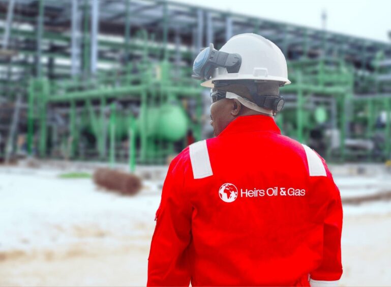 Man in red overall stands outside industrial facility