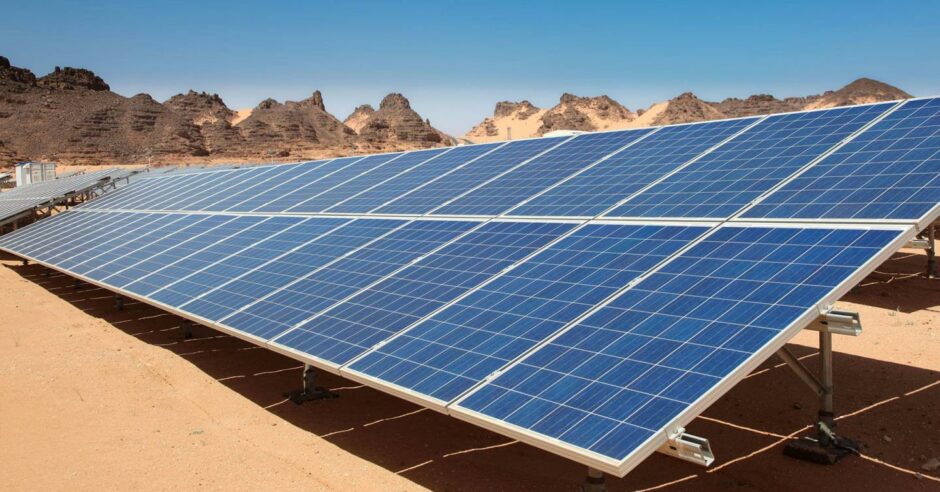 Solar panels in the desert, with a blue sky and mountains behind