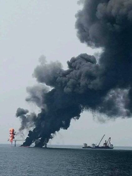 Black smoke billows from a facility offshore 