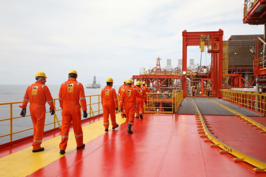 Workers in overalls walk along a red and yellow deck