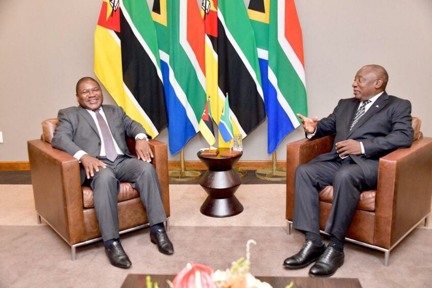 Two men sit on chairs with flags behind