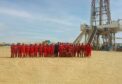 Work team in red overalls stand in the desert, in front of drilling rig