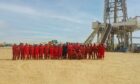 Savannah Energy team in red overalls stand in the desert, in front of drilling rig