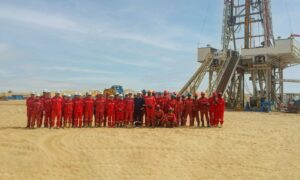 Work team in red overalls stand in the desert, in front of drilling rig