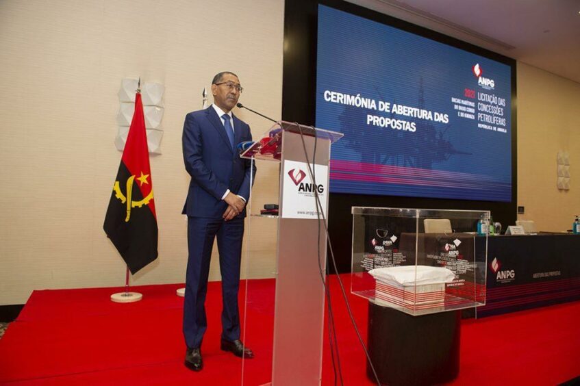 Man stands on stage in front of Angolan flag