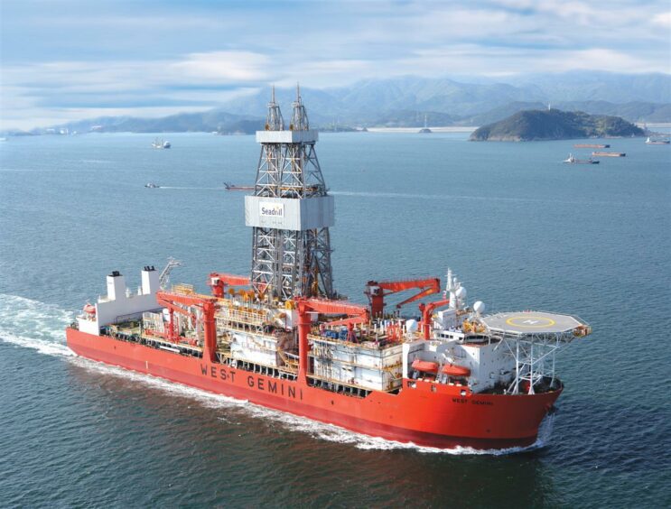 A red rig sails from left to right with an island in the back