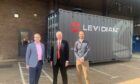 Three men stand in front of a shipping container