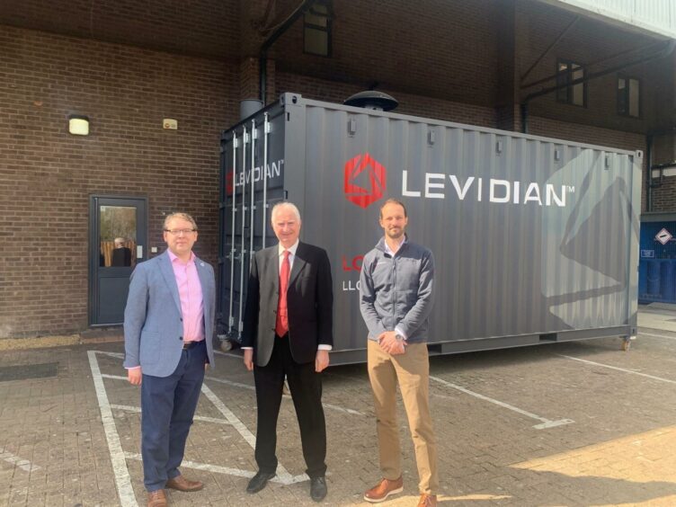 Three men stand in front of a shipping container