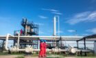 Workers in red under a blue sky, with pipelines behind