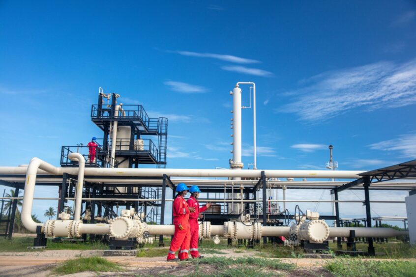 Workers in red under a blue sky, with pipelines behind