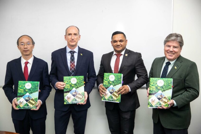 Four men in suits hold green document