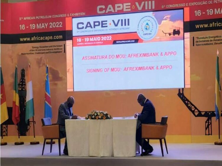 Two men sign documents at a table on a stage