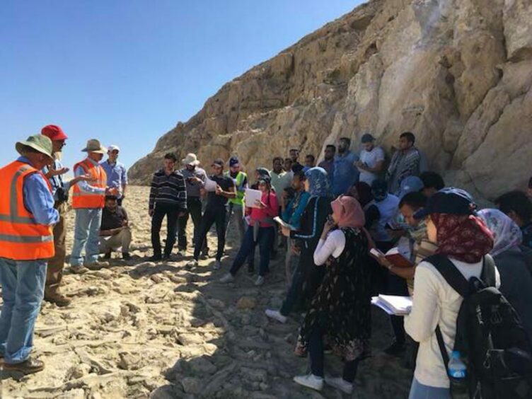 People in high vis vests talk to children in front of a cliff