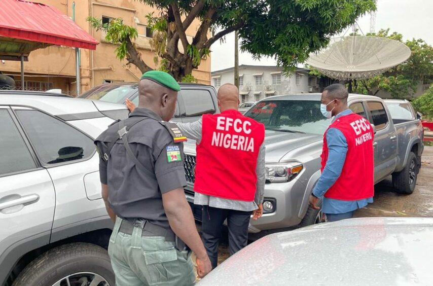 A police man and two EFCC agents walk past cars