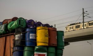 Oil barrels and a metro train in Faridabad, India, on Sunday, June 12, 2022. Extreme weather conditions in some nations, combined with Russia?s invasion of Ukraine, have led to a global squeeze in supplies of fossil fuels, and sent prices of oil, natural gas and coal soaring.
